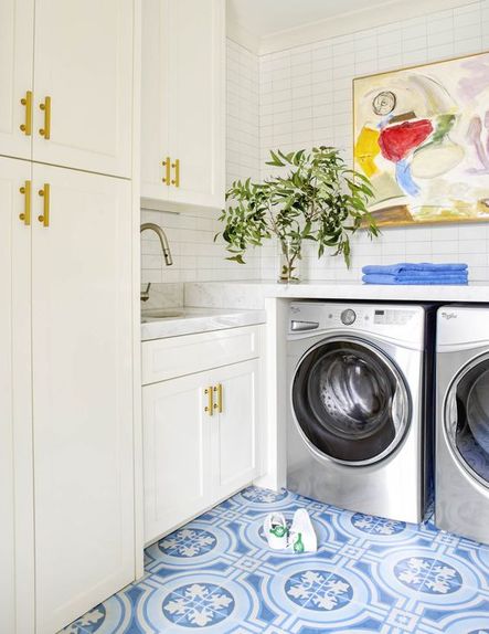 A blue tiled flooring in the laundry room balances with all-white cabinetry. Art pieces adorn the walls in multiple places throughout this home, but this is one of the most stunning. Abstract art is a great way to introduce color into a space.